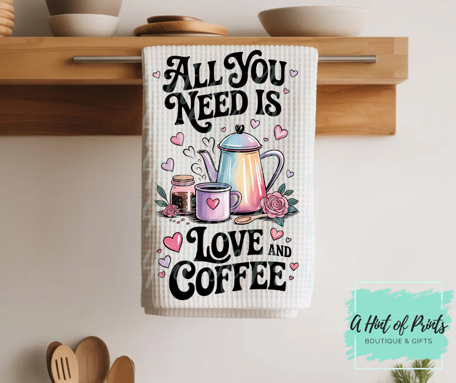 Kitchen towel with 'All You Need is Love and Coffee' text and graphics on a wooden shelf.